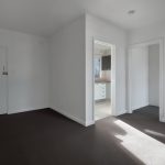 A corner of an empty new room with white walls, doors, and black floor